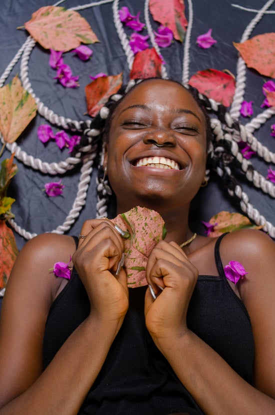 Person laying down smiling while holding a leaf surrounded by petals.